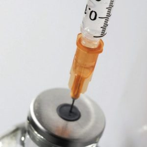 Insulin syringe puncturing a vial of compounded semaglutide